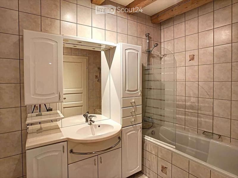 Bathroom with a white sink, mirror, bathtub, and shower area. The walls are tiled, and there are white cabinets and drawers.