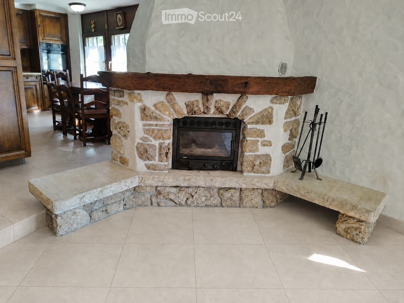 Stone fireplace with built-in seating, fireplace tools, and a dining area visible in the background.