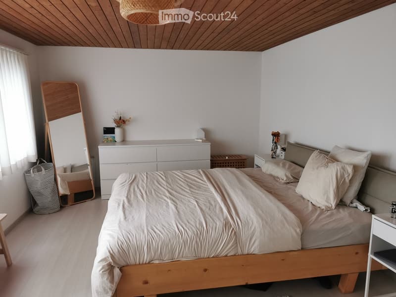 A modern, minimalist bedroom with a wooden bed, white bedding, a nightstand, a dresser, a mirror, and a vase on the dresser.