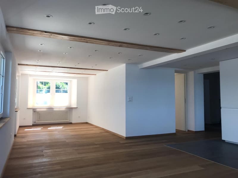 Empty room with wooden flooring, white walls, and recessed ceiling lights. Features large windows and a radiator under one window.