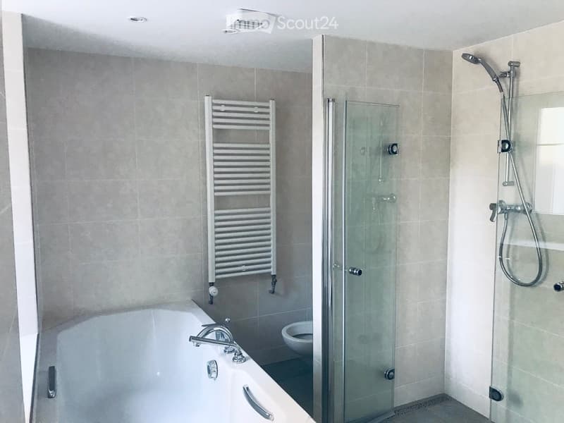 Modern bathroom with a bathtub, glass-enclosed shower, toilet, and a radiator. Light-colored tiles and sleek fixtures.