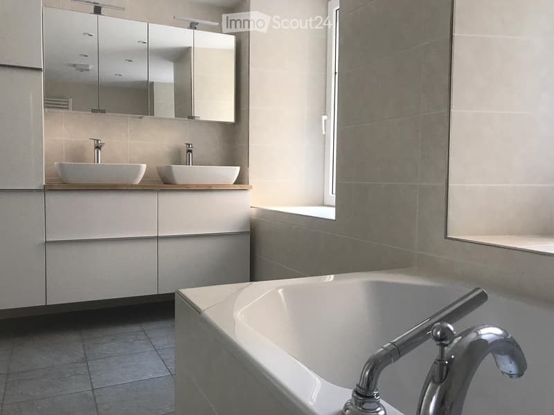 Modern bathroom with a bathtub, two sinks, a large mirror, and a window with floral-patterned tiles.