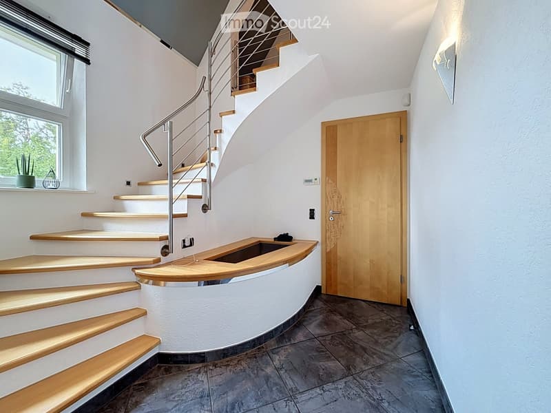 Spiral staircase with wooden steps and metal railing, white walls, large window, wooden door, and small shelf with decorative items.