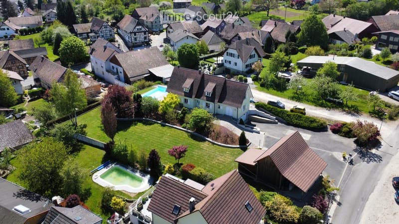 Aerial view of a residential neighborhood with multiple houses, gardens, and a swimming pool visible in one of the yards.