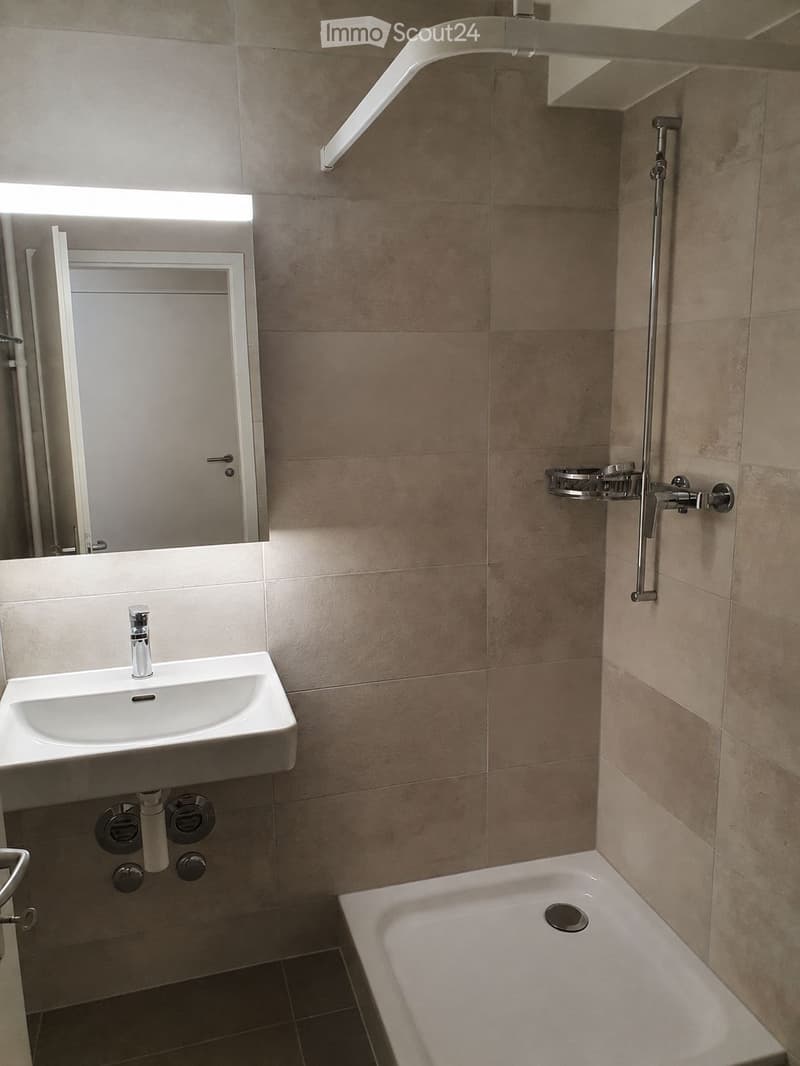 Modern bathroom with a white sink, bathtub, and built-in shower area. Features a large mirror with built-in lighting and a sleek chrome showerhead with a rail.