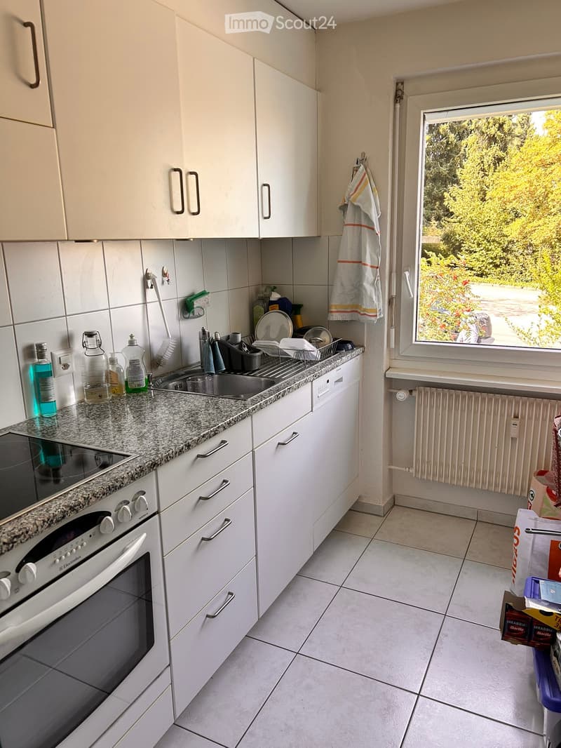 Modern kitchen with white cabinets, granite countertop, stainless steel sink, oven, and dishwasher. A window offers a view of greenery outside.