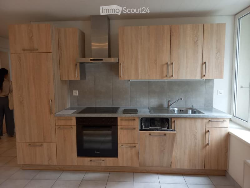 Modern kitchen with light wood cabinets, stainless steel appliances, and a grey tiled backsplash.