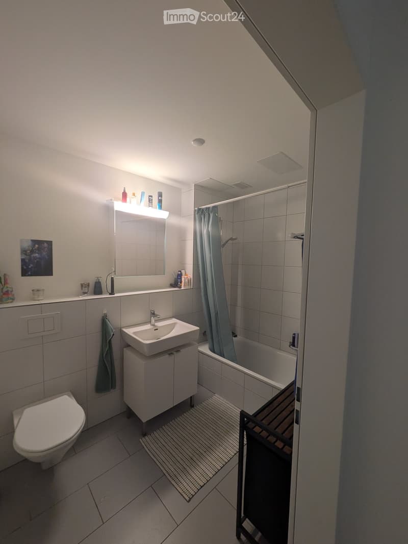 Modern bathroom with a toilet, sink, bathtub, and mirror. Features a built-in cabinet under the sink, a towel hanging on the wall, and a shower curtain in the bathtub area.
