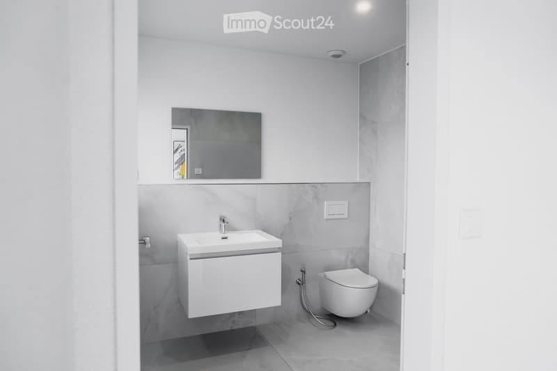 Modern bathroom with white sink, mirror, and toilet, featuring grey marble tiles and sleek fixtures.