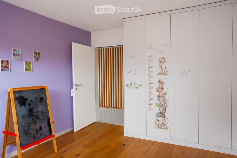 Child-friendly room with purple walls, wooden floor, white closet with animal-themed height chart, blackboard on easel, and several picture frames on the wall.