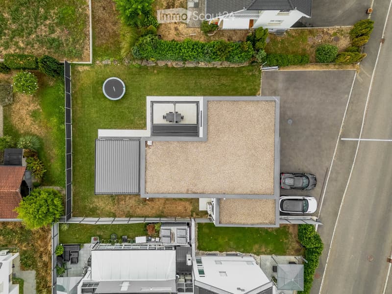 Aerial view of a modern house with a well-maintained garden, patio area, and parking space for two cars.