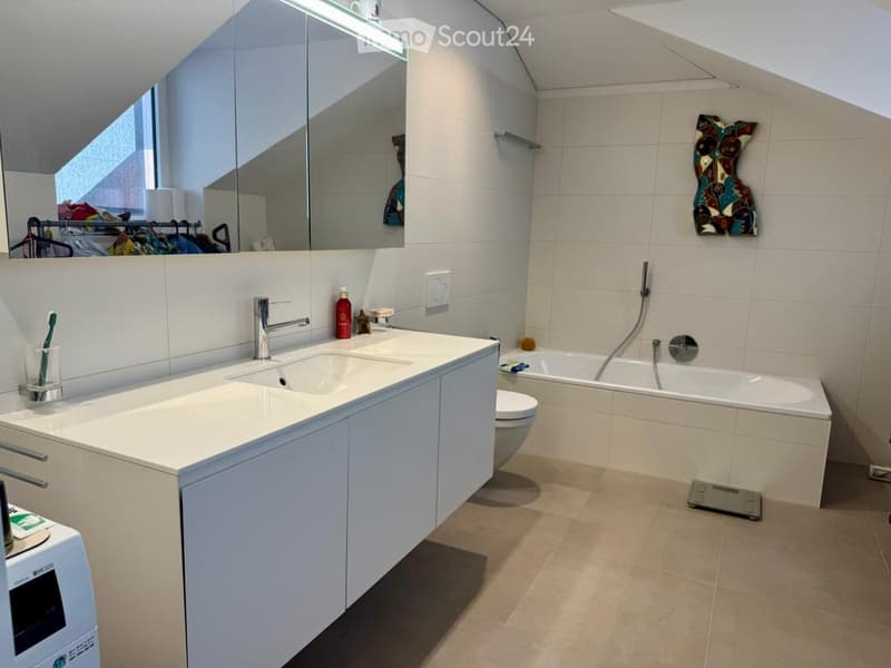 Modern bathroom with white tiles, double sink, bathtub, and a large mirror. Includes a toothbrush holder, bottle, and decorative wall art.