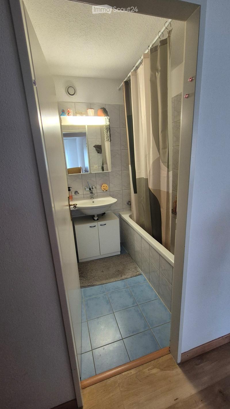 Bathroom with a sink, mirror, cabinet, bathtub, and shower curtain. The floor is tiled, and the walls are tiled with a mix of light and dark tiles.