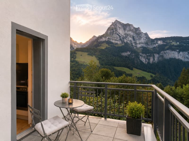 Balcony with a scenic mountain view, featuring a small round table, two white cushioned chairs, and potted plants.