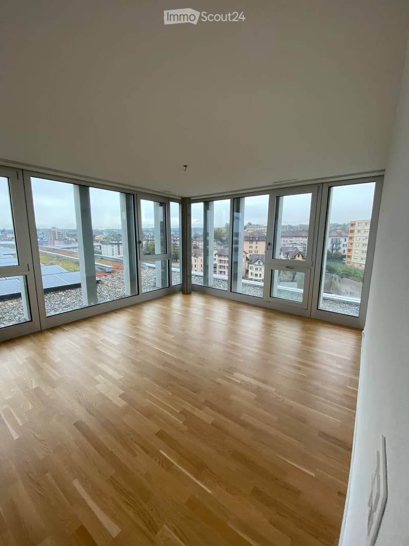 Completely empty room with wooden flooring and large windows offering a cityscape view.