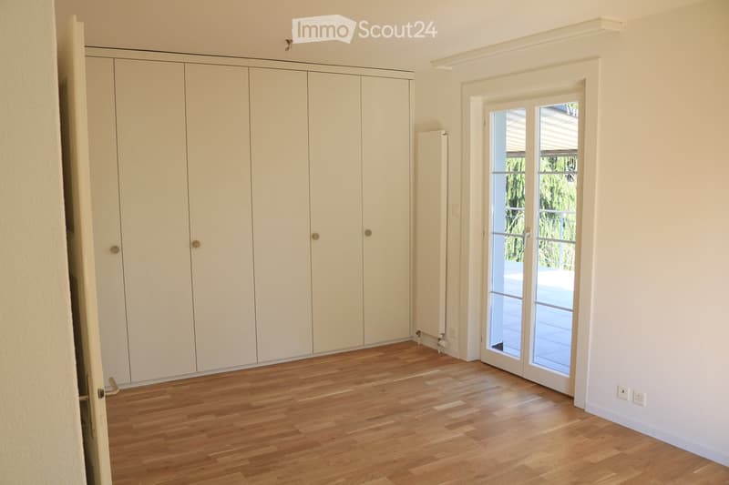Empty room with light wooden flooring, white walls, large built-in wardrobe, and a sliding glass door leading to a balcony or outdoor area.
