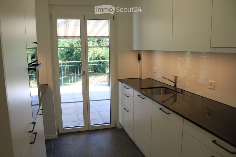 Modern kitchen with white cabinets, dark countertops, a sink with a faucet, and an oven. Features a large glass door leading to a balcony.