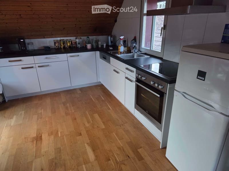 Modern kitchen with white cabinets, wooden flooring, stainless steel appliances including a refrigerator, oven, and sink, and various kitchen items on the counter.