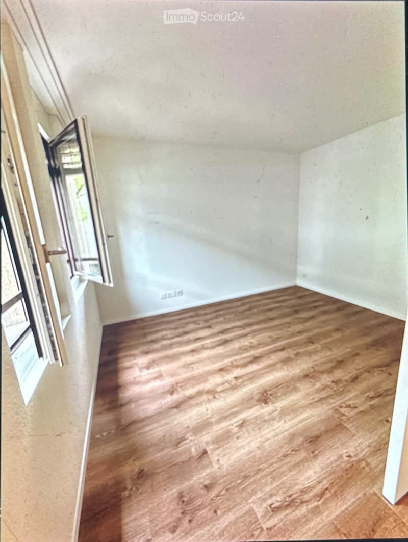 Empty room with wooden flooring and white walls, featuring a partially open door with glass panels.