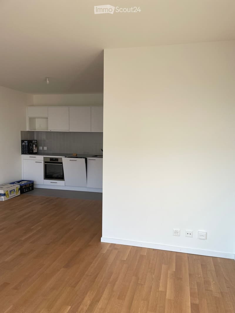 Empty kitchen with white cabinets, stainless steel appliances, and wooden flooring.