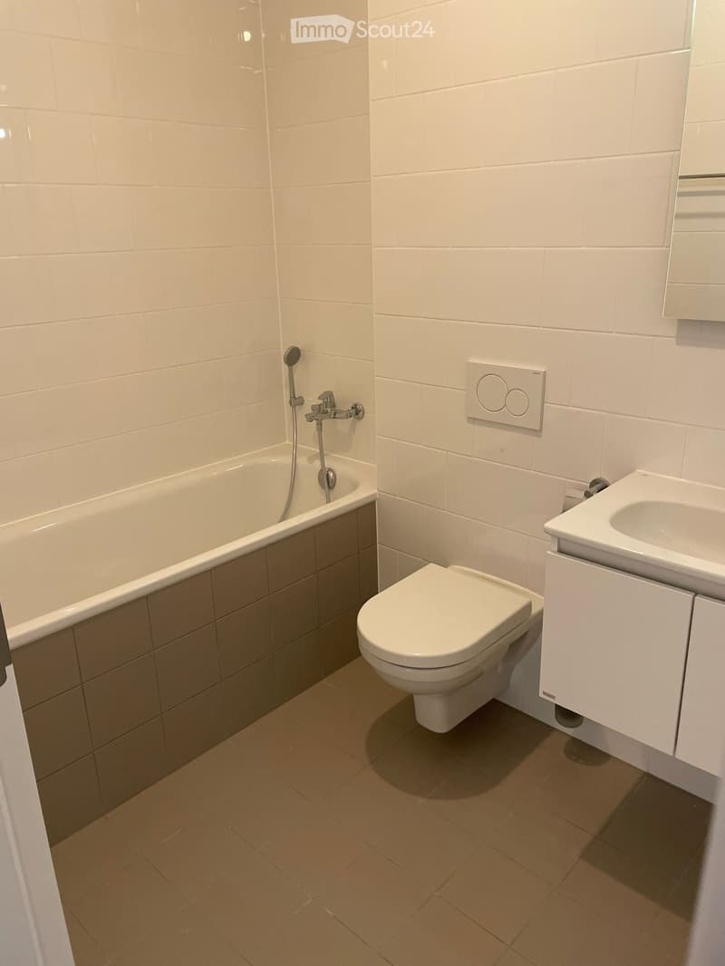Modern bathroom with white tiles, bathtub, toilet, sink, and showerhead.