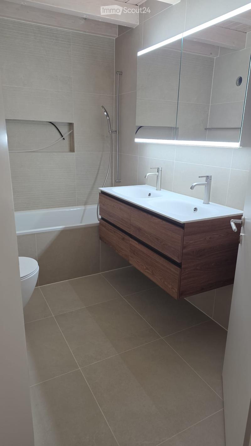 Modern bathroom with a bathtub, sink, toilet, and a glass-enclosed shower area. Features a wooden vanity with a white countertop and silver faucets.