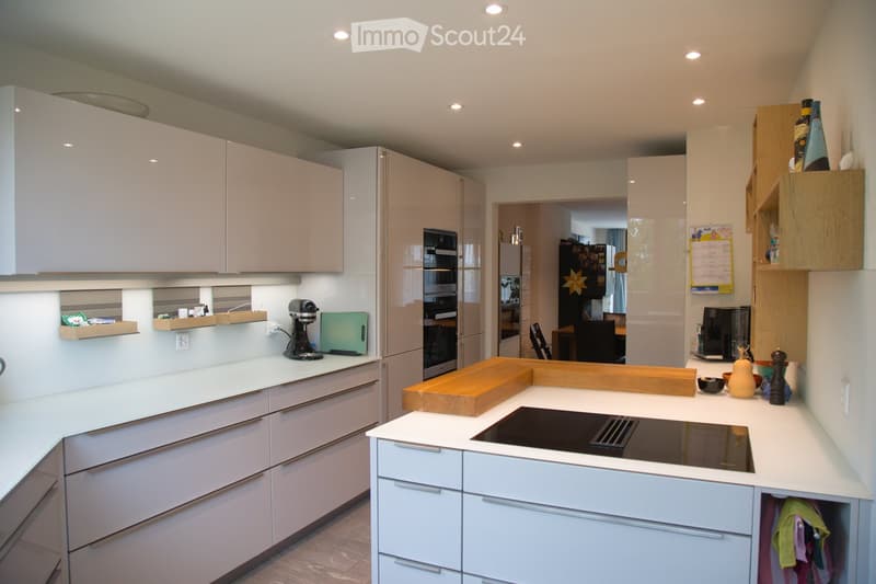 Modern kitchen with white cabinets, an induction stove, and various appliances including a refrigerator, microwave, and coffee maker. The kitchen features a central island with a wooden cutting board and a bowl on the counter.