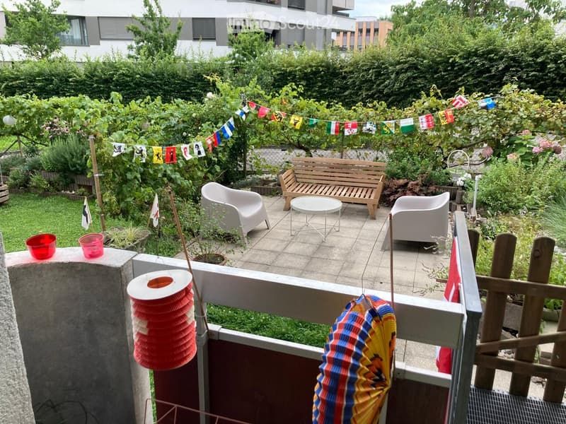 Balcony with a wooden bench, white chairs, a small round table, and colorful flags and decorations.