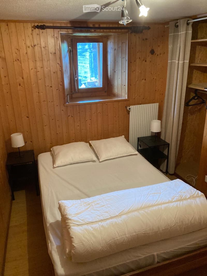Cozy bedroom with wooden walls, a large bed with white bedding, two nightstands with lamps, and a window offering a view.