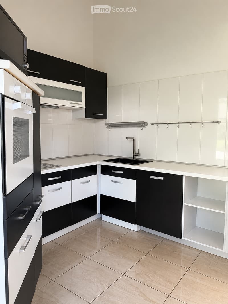 Modern kitchen with white and black cabinets, a sink with a faucet, and an oven. The floor is tiled in a light beige color.