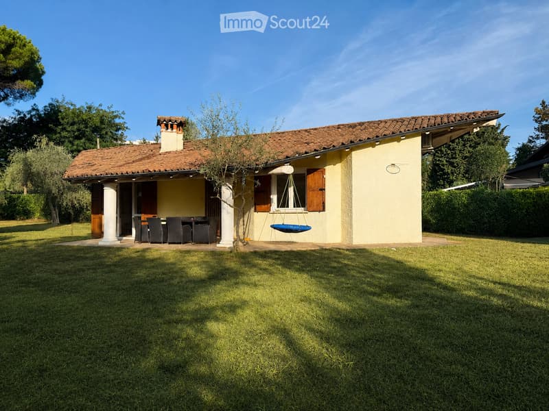 Single-story house with a tiled roof, light yellow walls, and a covered patio area with a dining set and hanging chair.