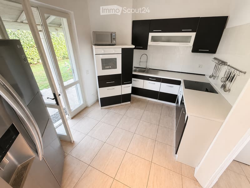 Modern kitchen with black and white cabinets, stainless steel appliances, and a large window leading to a garden.