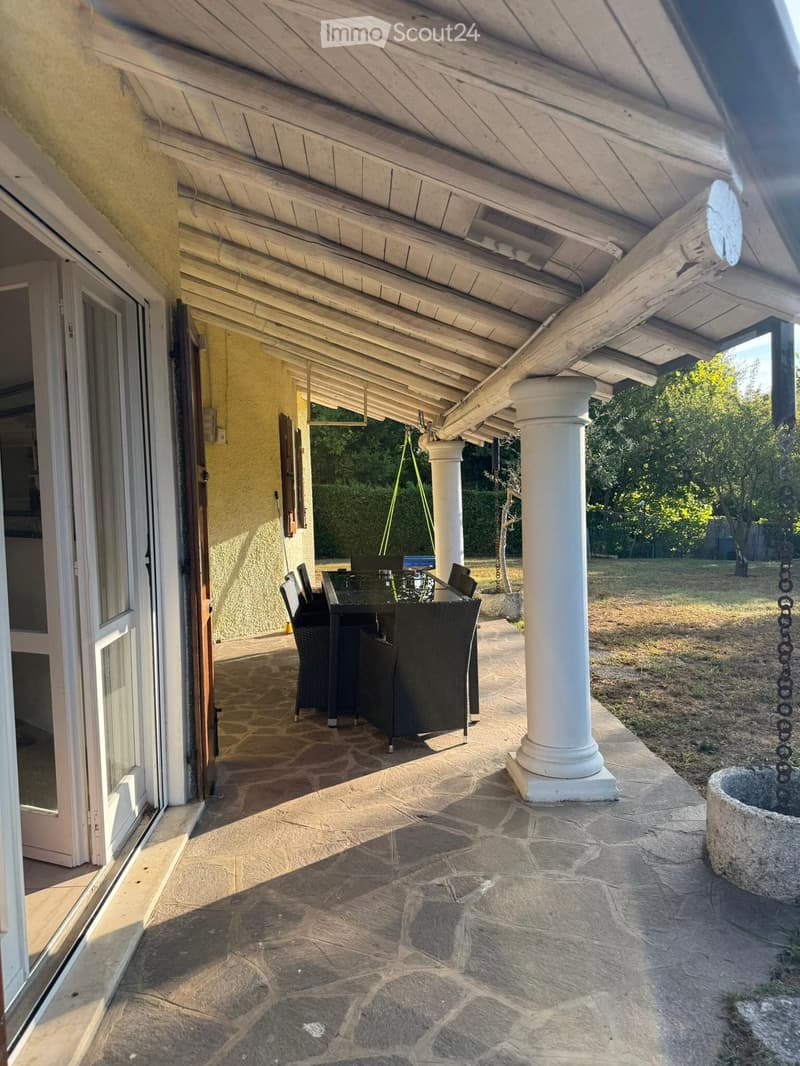 Covered outdoor patio with stone flooring, white columns, and a dining set including a table and chairs.