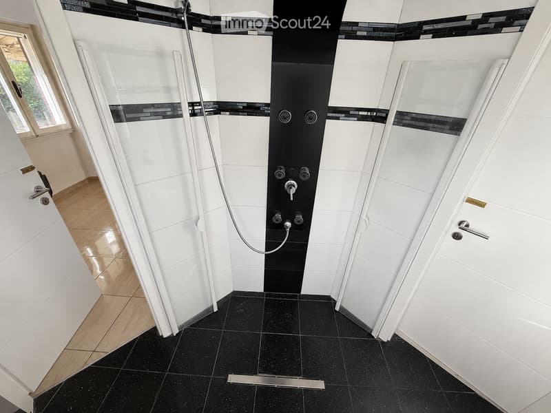Modern bathroom with black and white tiles, glass shower stall, and white cabinets.