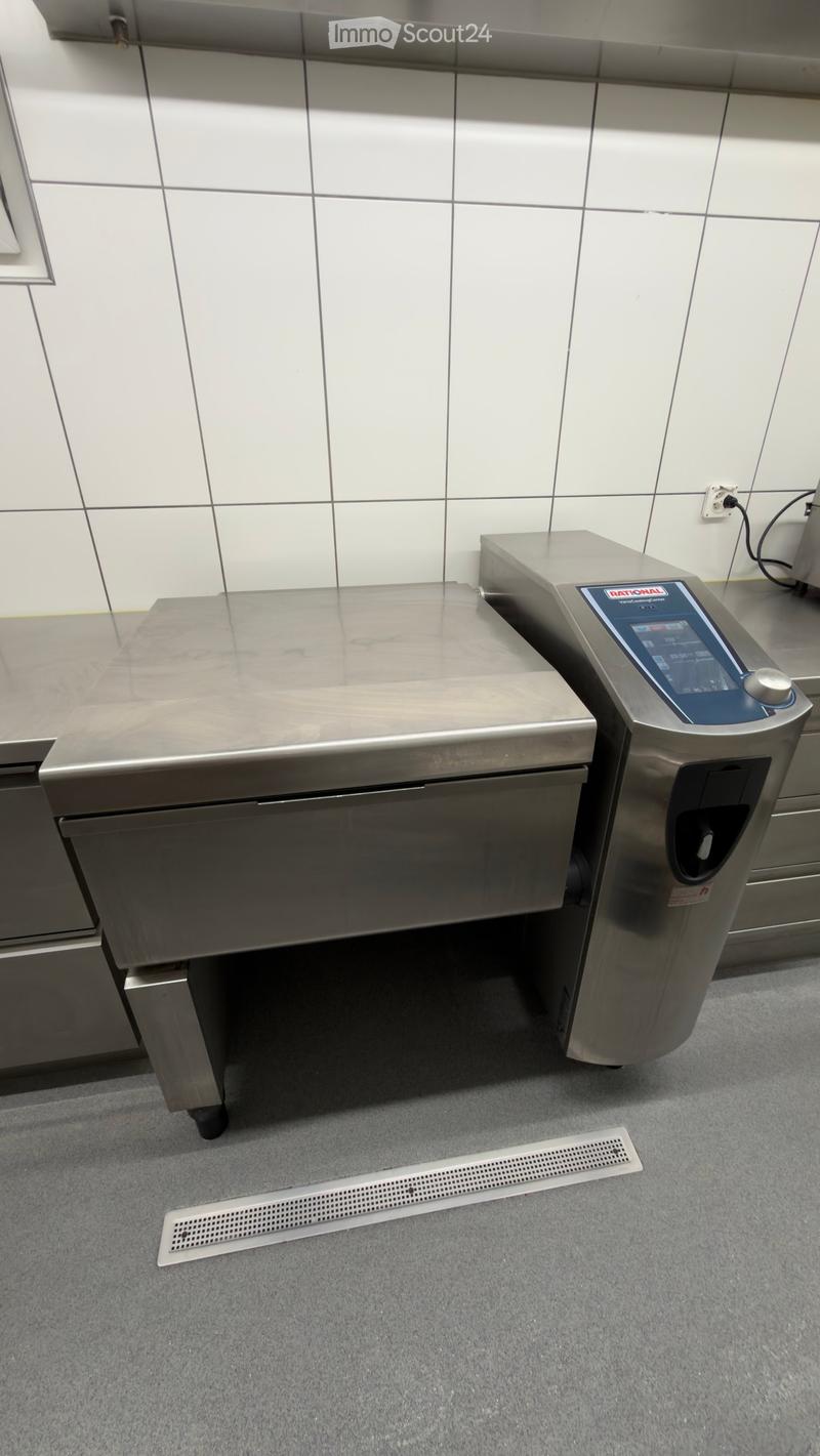 Stainless steel kitchen counter and appliance with digital interface, tiled walls, and a floor drain.