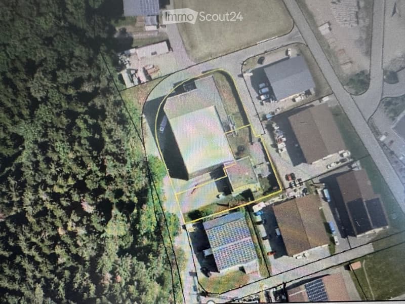 Aerial view of a residential property with multiple buildings, including a main house, garage, and outbuildings, surrounded by trees and a driveway.