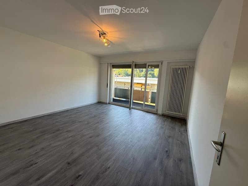 Empty room with wooden flooring, white walls, and a sliding glass door leading to a balcony area.