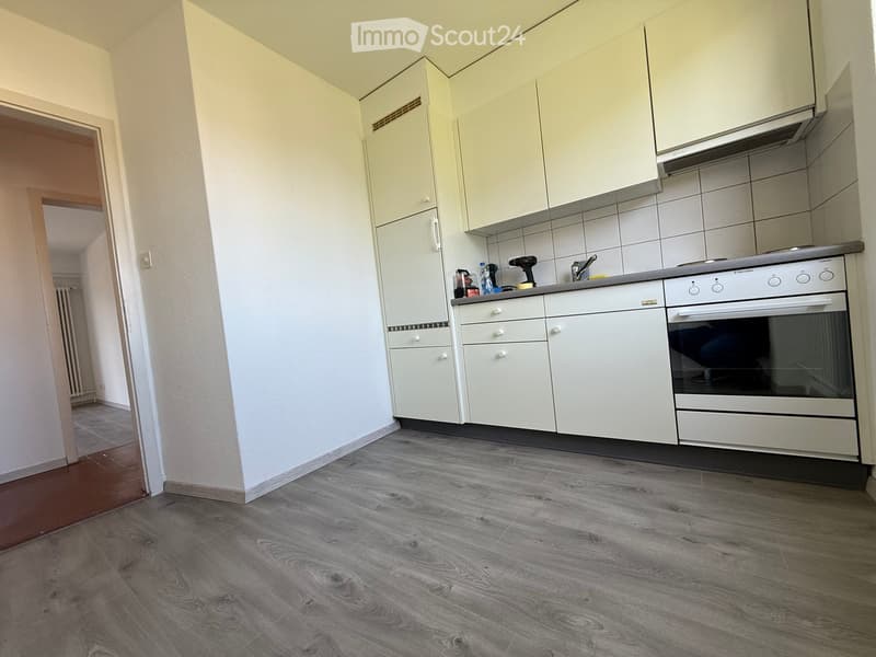Modern kitchen with white cabinets, grey countertop, and a built-in oven. Wooden flooring and tiled backsplash.