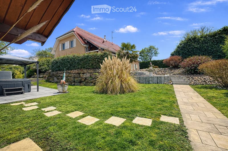 Well-maintained garden with a lawn, stone pathway, decorative plants, a hot tub, and a covered patio area.