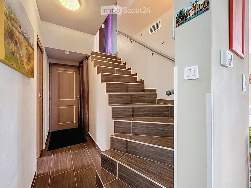 Modern hallway with wooden tiled flooring, staircase with wooden steps and metal railing, white walls, and framed artwork.