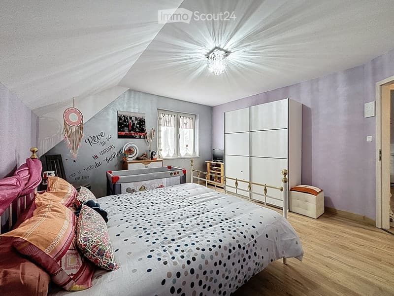 Cozy bedroom with a large bed, pillows, and a blanket, a wardrobe, a small table with a mirror, and a dreamcatcher hanging on the wall.