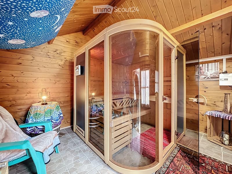 Wooden bathroom with a sauna, a small table with a lamp, a chair, and a mirror.