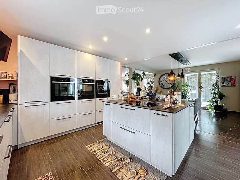 Modern kitchen with white cabinets, stainless steel appliances, island, and pendant lights. Includes a clock, blender, and decorative items on the counter.