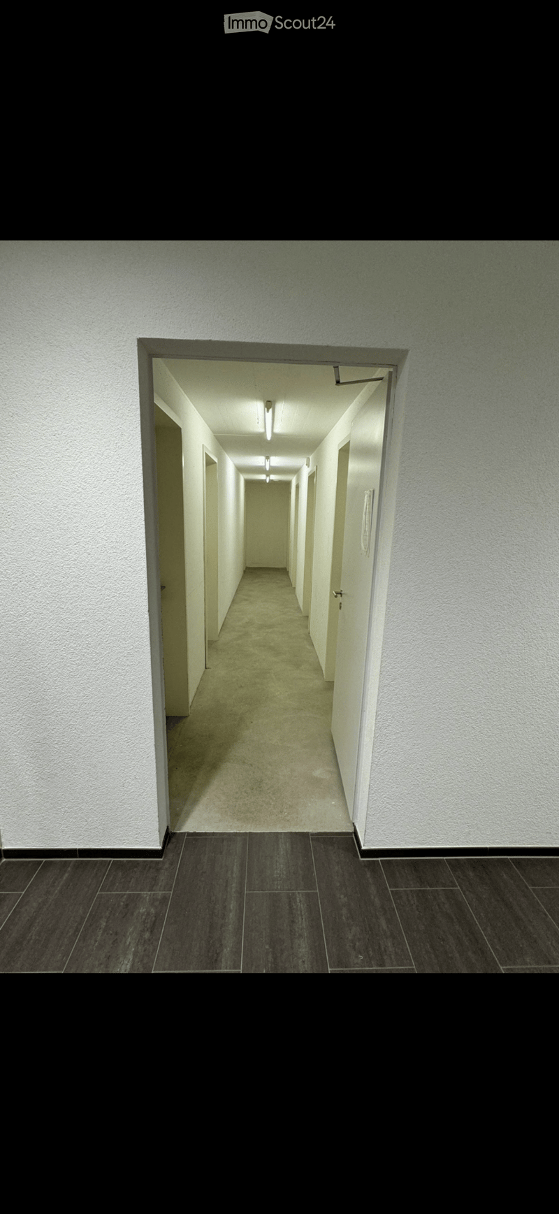 Empty hallway with white walls, dark tiled floor, and multiple doors on both sides.