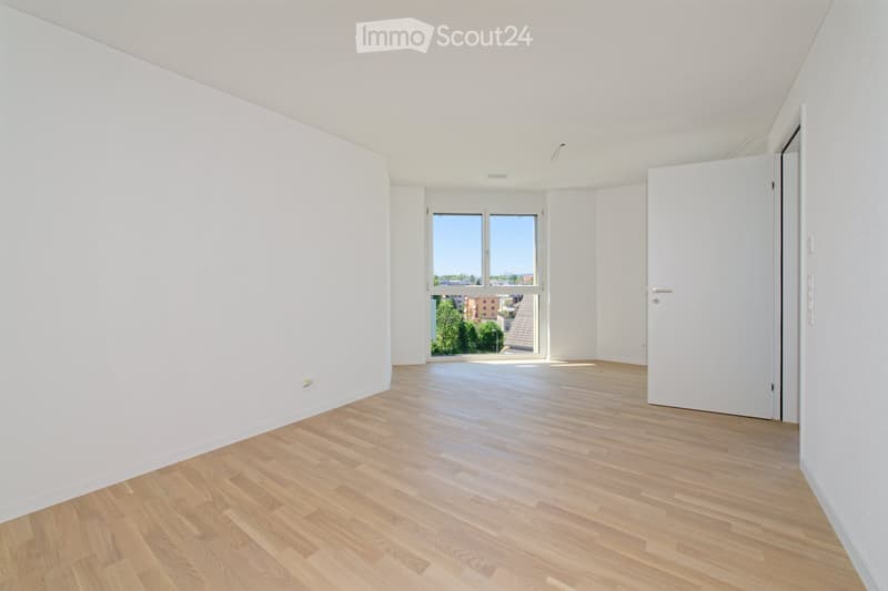 Empty room with white walls, wooden flooring, and large windows offering a view of the outside. No furniture or equipment is present.