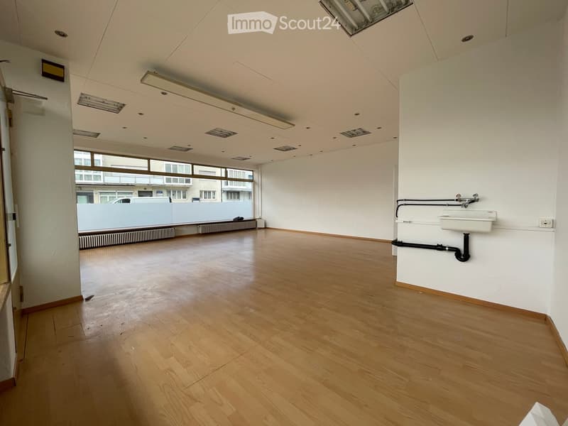 Empty room with wooden flooring, white walls, and a sink in the corner. Large windows provide natural light.