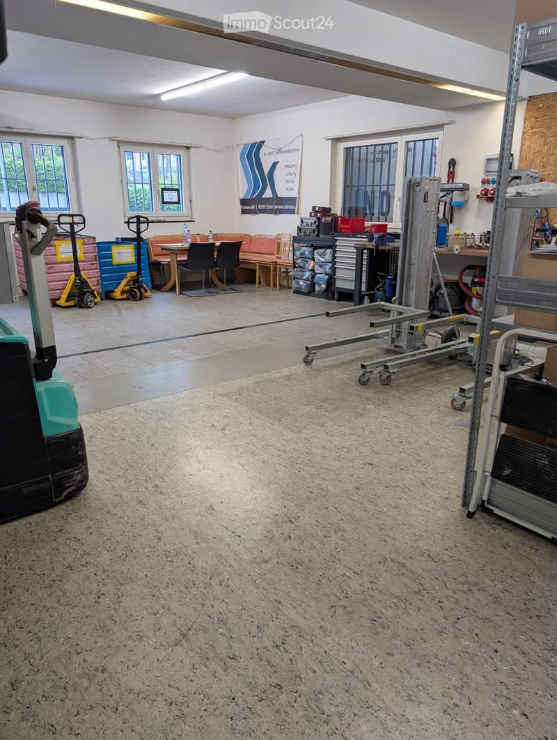 Workshop or garage area with a sofa, table, chairs, workbench, storage units, and handcart.