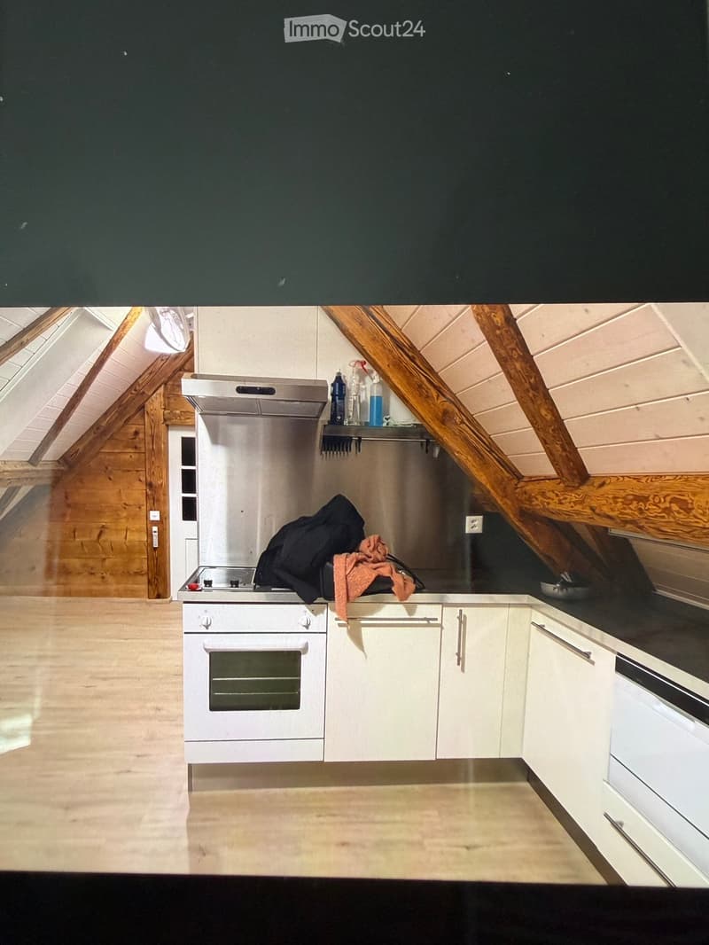 Modern kitchen with white cabinets, stainless steel appliances, and wooden beams on the ceiling. A jacket and oven mitt are placed on the counter.
