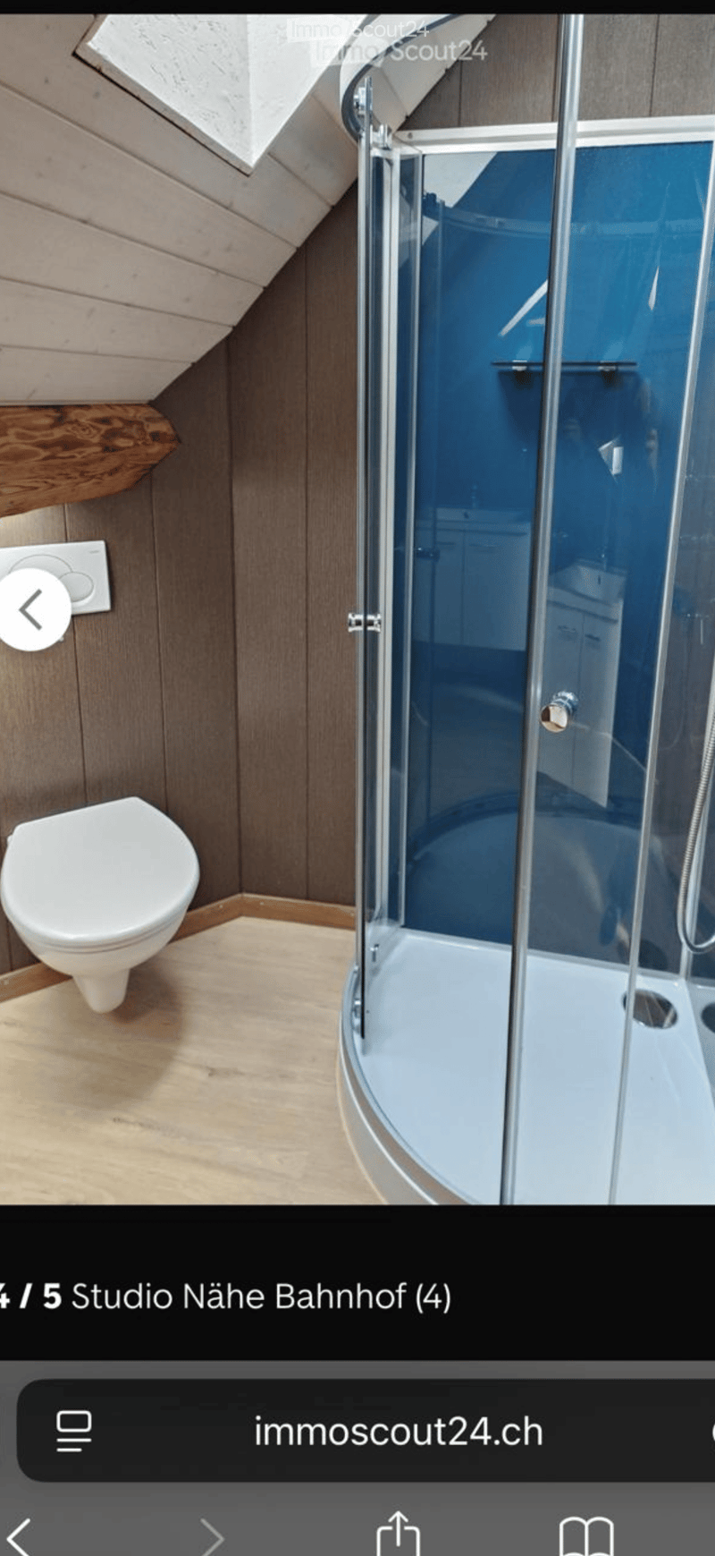 Modern bathroom with wooden walls, a white toilet, and a glass-enclosed shower with blue tiles.