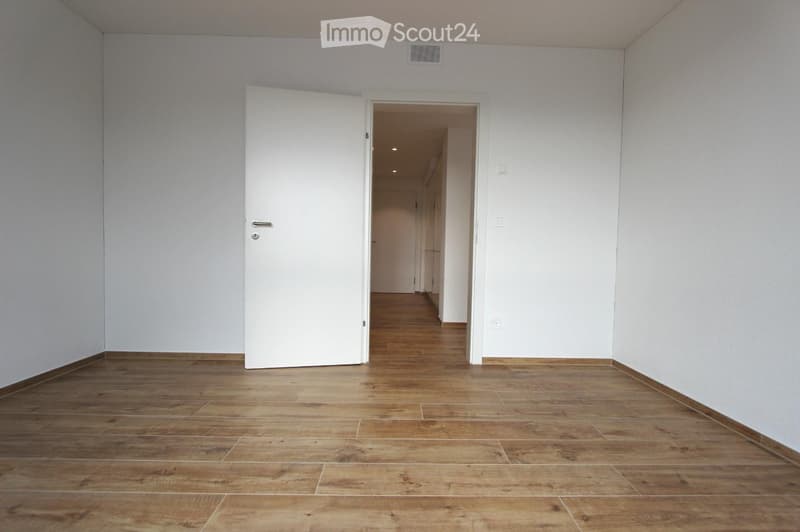 Empty room with wooden flooring and white walls, featuring an open doorway leading to another area.
